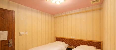 Una habitación con dos camas, una puerta de madera y una lámpara en el techo.