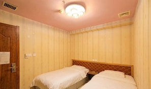 Una habitación con dos camas, una puerta de madera y una lámpara en el techo.