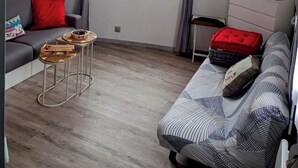 A modern living room with a grey sofa, a red cushion, a patterned sofa, a small table with baskets, and a TV on a stand.