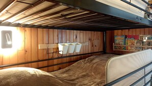 A bunk bed room with wooden walls, a metal headboard, and a shelf with children's books.
