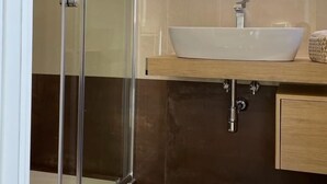 A modern bathroom with a glass shower enclosure, a white sink, and a wooden vanity. - B&B Jerocades (Parghelia)
