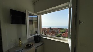 A small kitchen with a window, a flat-screen TV, a bottle of wine, and a plate of food. - B&B Jerocades (Parghelia)