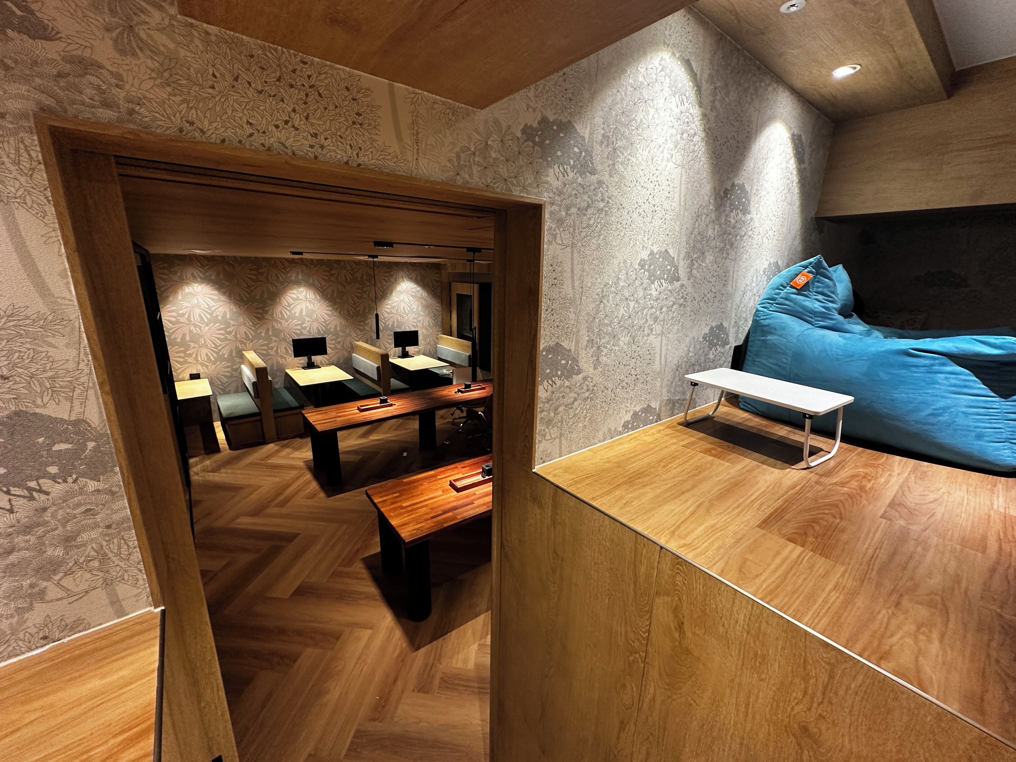 A modern room with wooden furniture, a blue bean bag, and patterned wallpaper.