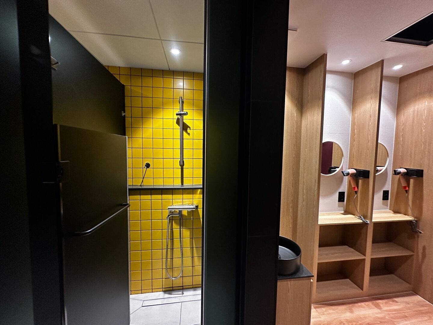 Une salle de bain moderne avec des murs recouverts de carreaux jaunes, un espace douche et des meubles en bois dotés de miroirs.