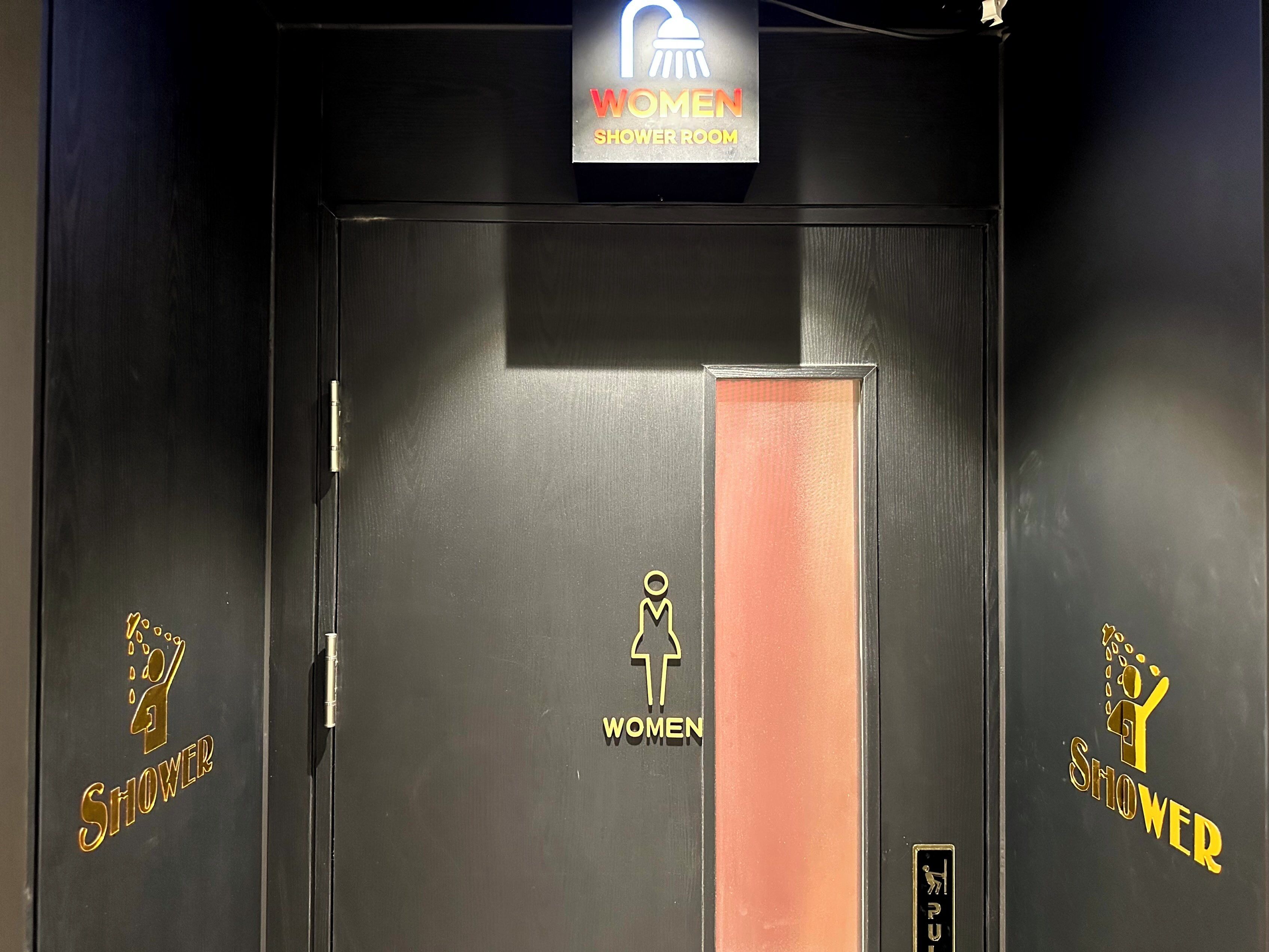 Baño de mujeres con un cartel sobre la puerta y un tirador.