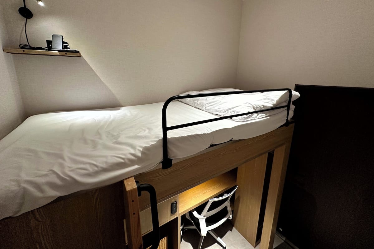 A bunk bed with a desk underneath, a shelf with a lamp, and a television.