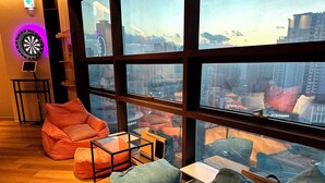 Ein modernes Wohnzimmer mit großen Fenstern, einer Dartscheibe und Blick auf die Stadt.