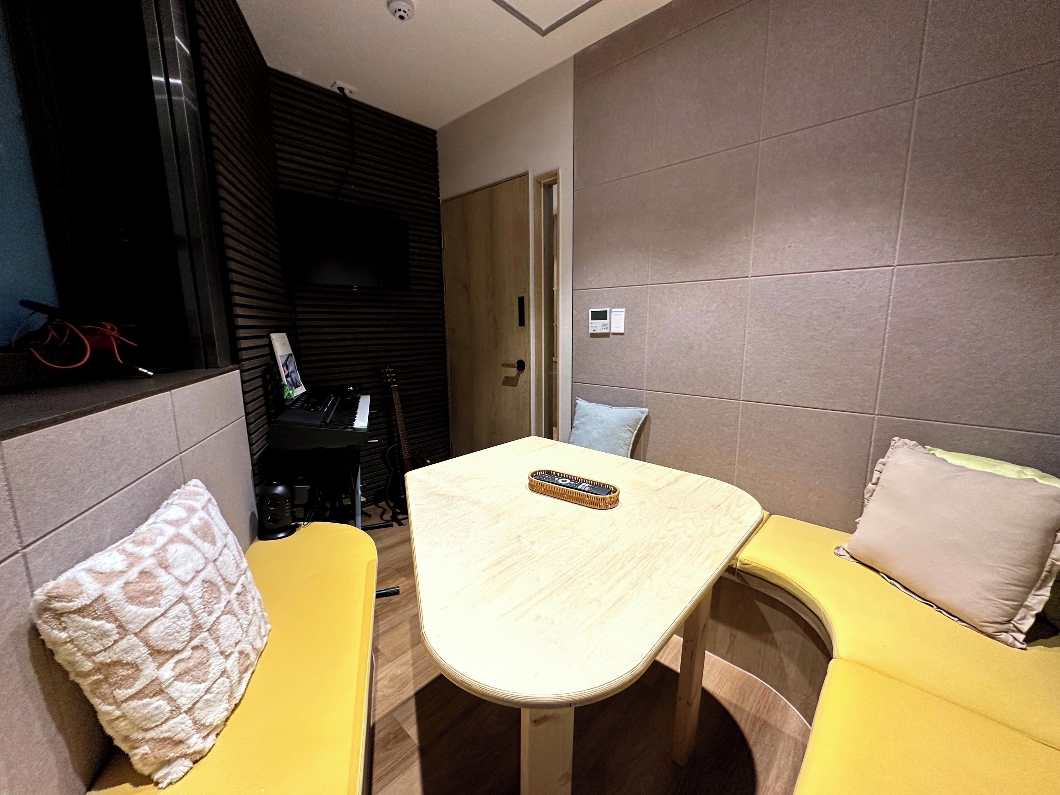 A compact living space with a small table and two yellow sofas, a black piano, and a guitar in the background.