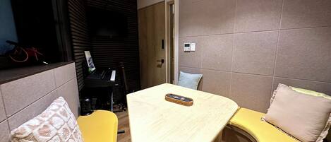 A compact living space with a small table and two yellow sofas, a black piano, and a guitar in the background.