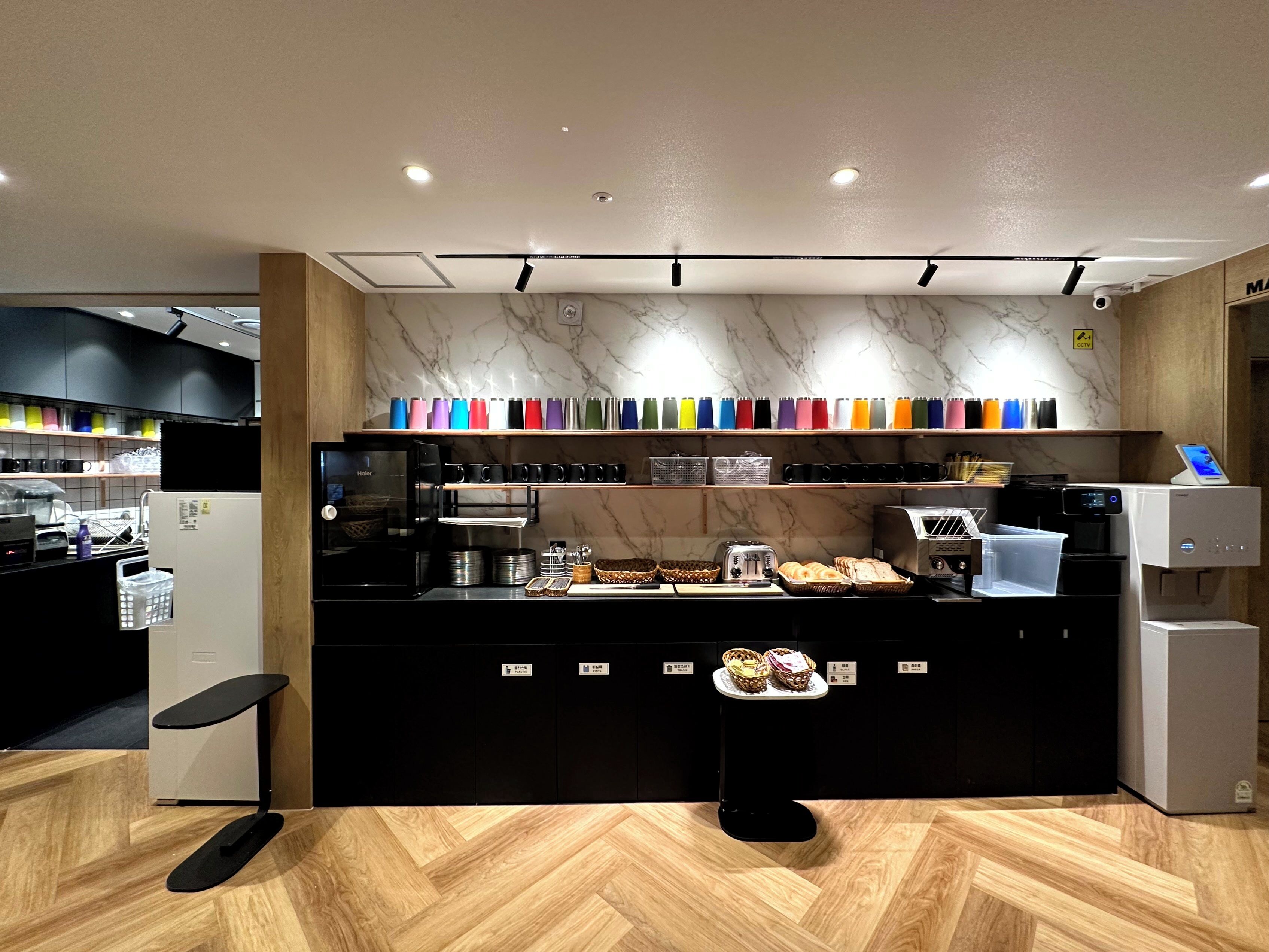A modern cafe with a marble wall, a coffee machine, and a variety of colorful cups on display.