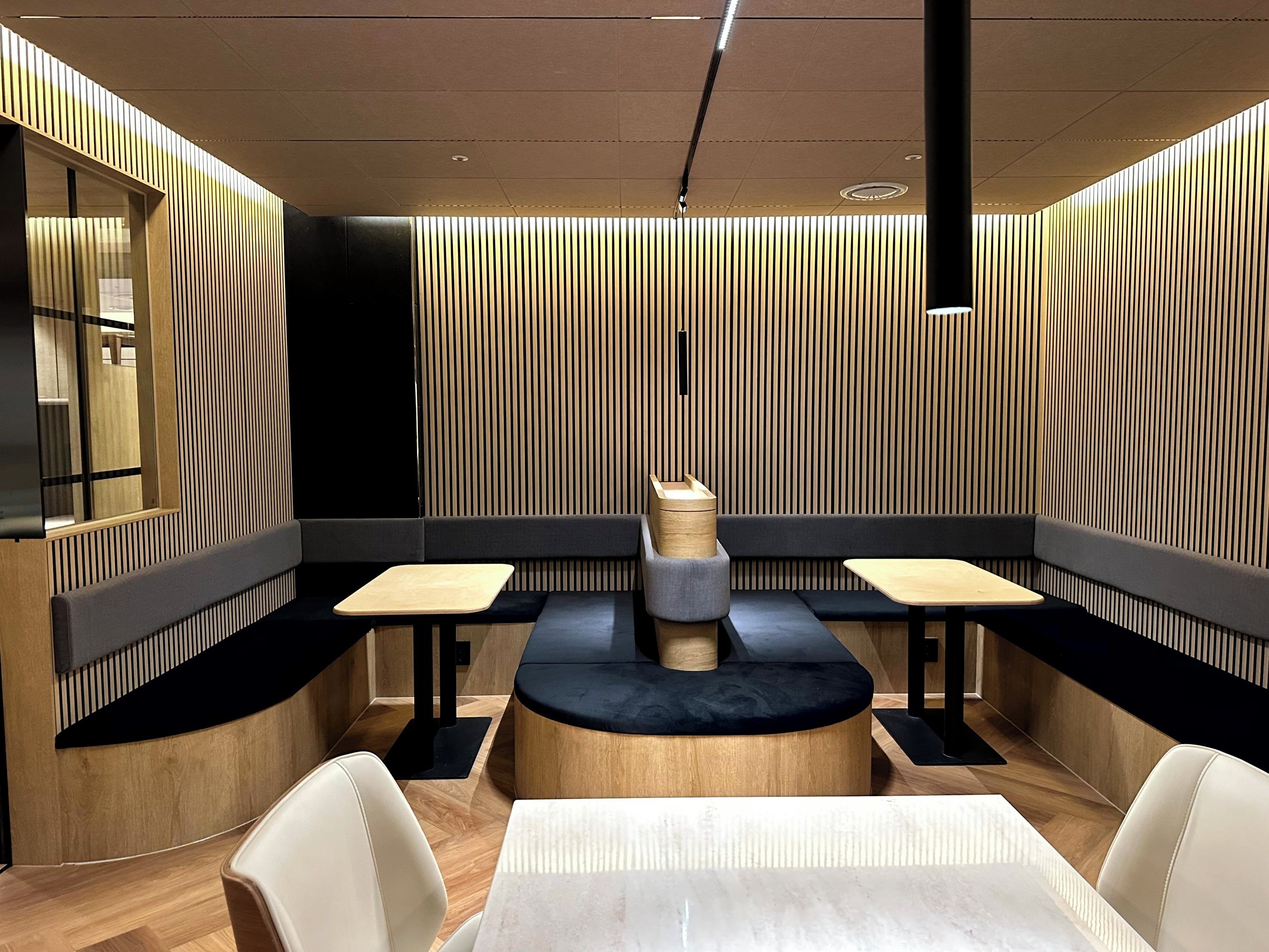 Un intérieur de restaurant moderne avec une table ronde centrale, des banquettes et un plafond haut doté d’un éclairage encastré.