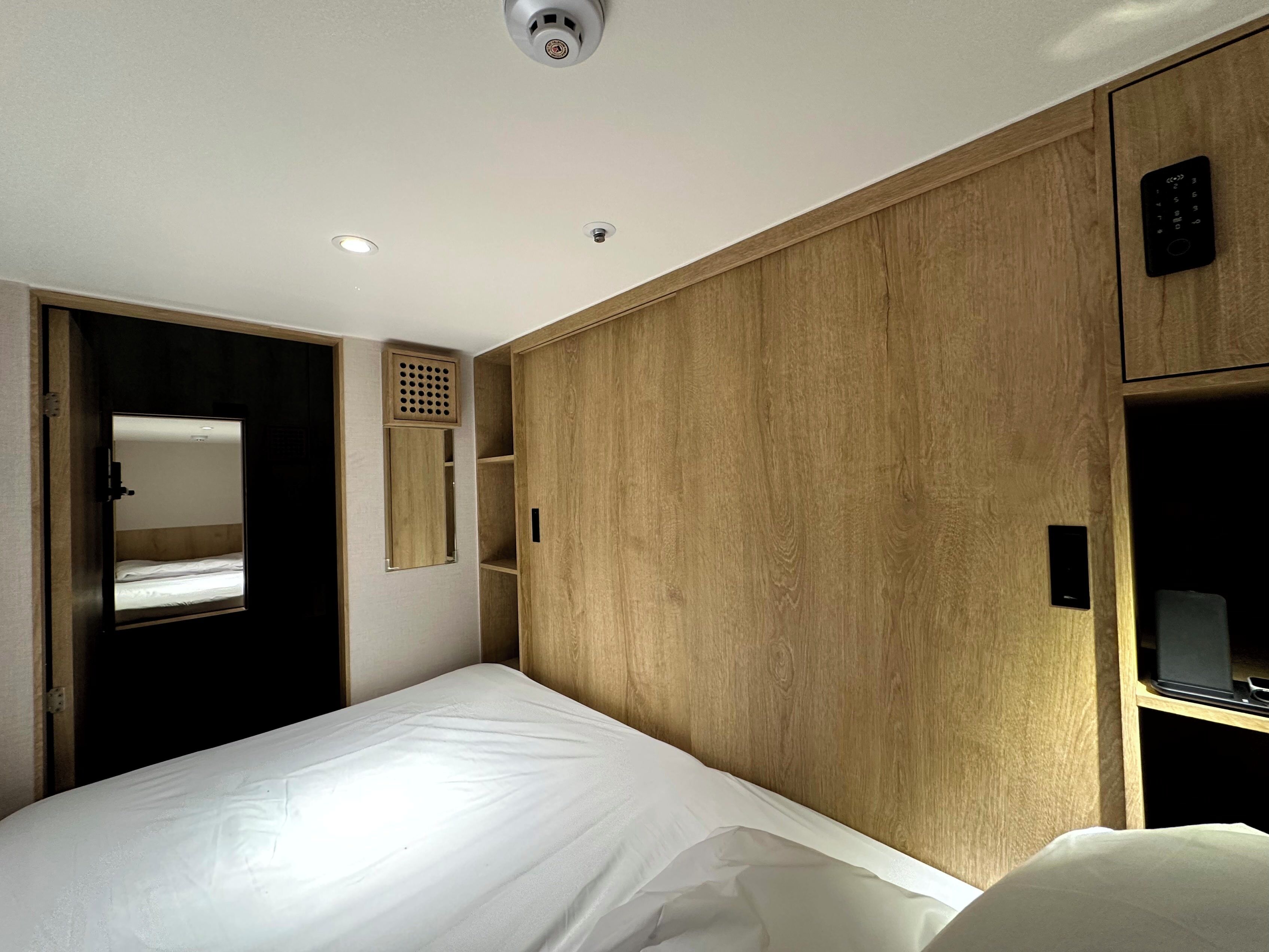 Een hotelkamer met een bed, een houten garderobe, een klein plankje en een spiegel.