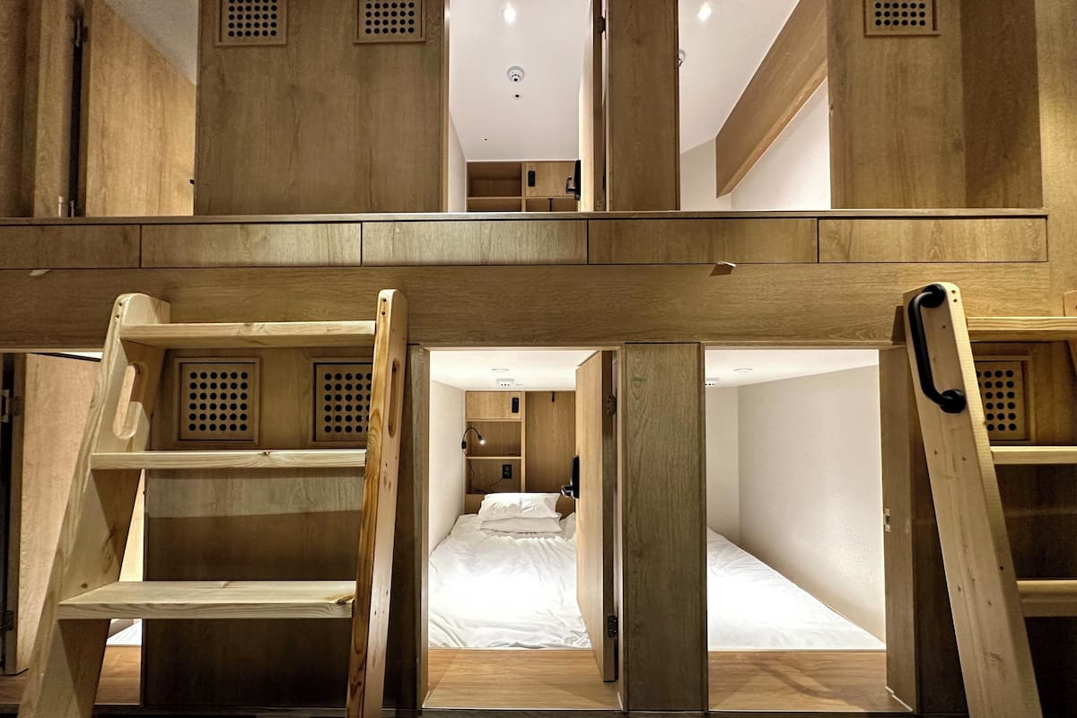 A room with bunk beds and a ladder, wooden walls, and a ceiling with ventilation.