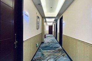 Hotellets gang med et mønstret gulvtæppe, døre på hver side og en lampe i loftet.