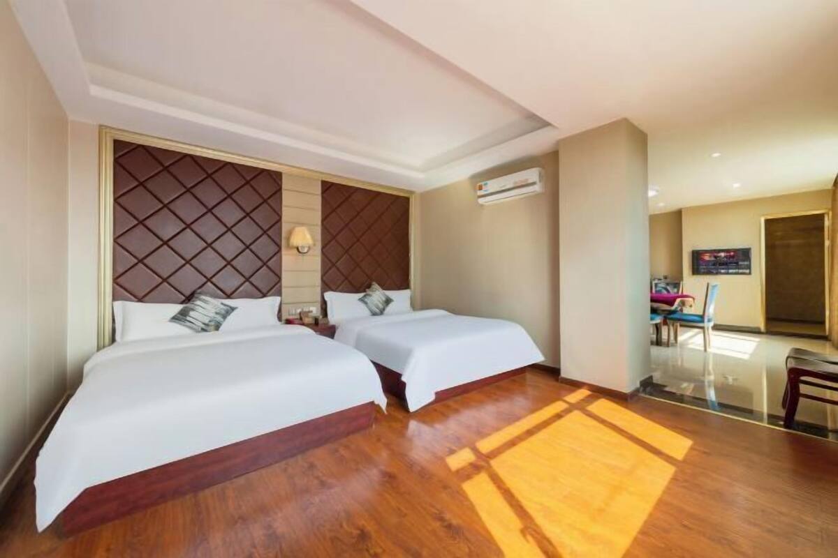 A hotel room with two beds, a wooden floor, a wall-mounted air conditioner, and a TV.