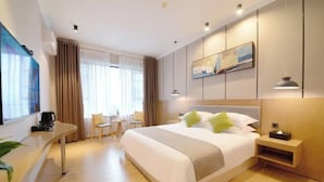 A modern hotel room with a large bed, a desk with a coffee maker, a seating area with chairs, and a painting on the wall. - Shengshi Hotel (Zengcheng Donghuicheng Wanda Store) (Guangzhou)