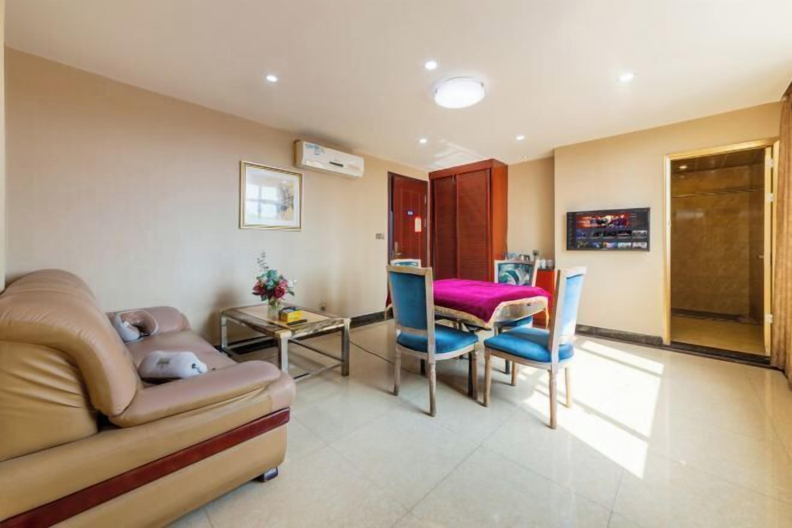 A hotel room with a sofa, two chairs, a small table with a vase, and a TV on the wall.