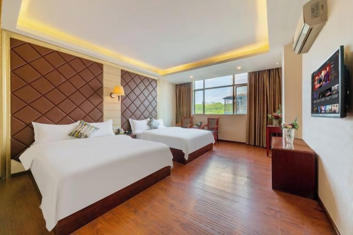A hotel room with two beds, a TV, a window with curtains, and a wooden floor.