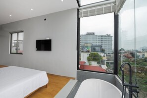 Une chambre moderne dotée d’une grande fenêtre, d’un téléviseur à écran plat et d’une baignoire.