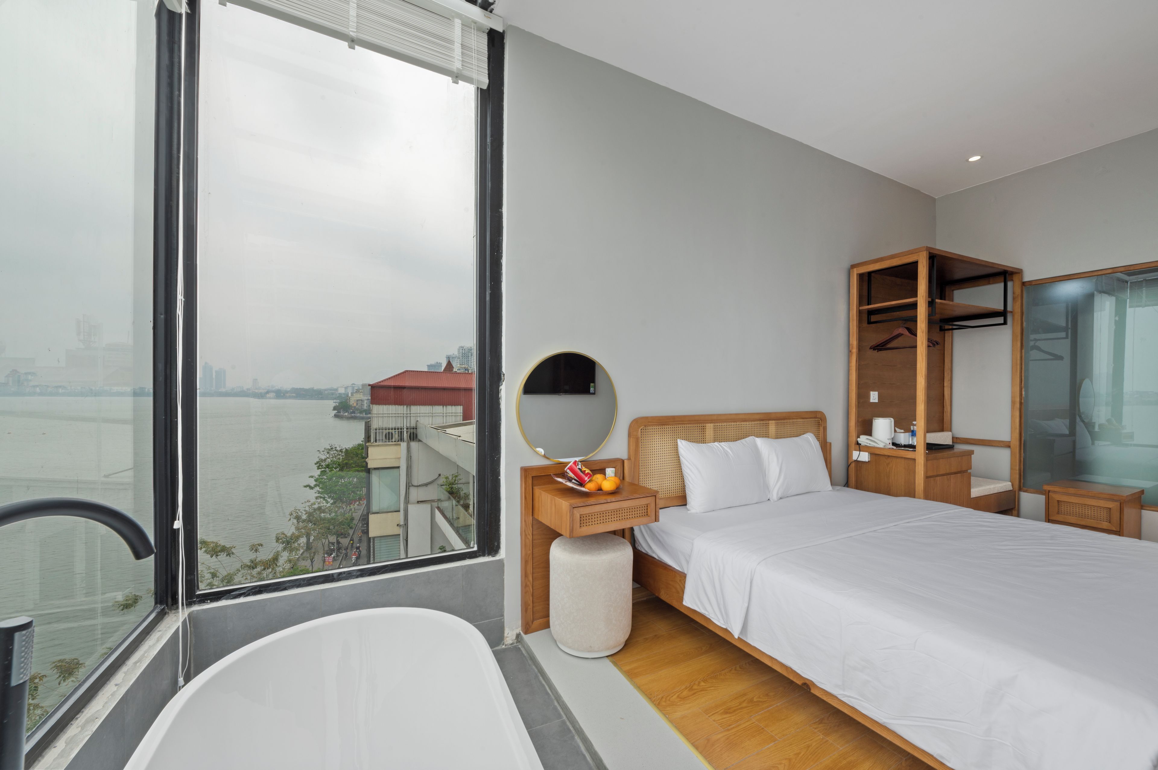 Een moderne hotelkamer met een groot raam, een bed, een nachtkastje met spiegel, een houten garderobe en een bad.