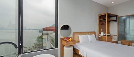 Une chambre d’hôtel moderne dotée d’une grande fenêtre, d’un lit, d’une table de chevet avec un miroir, d’une armoire en bois et d’une baignoire.