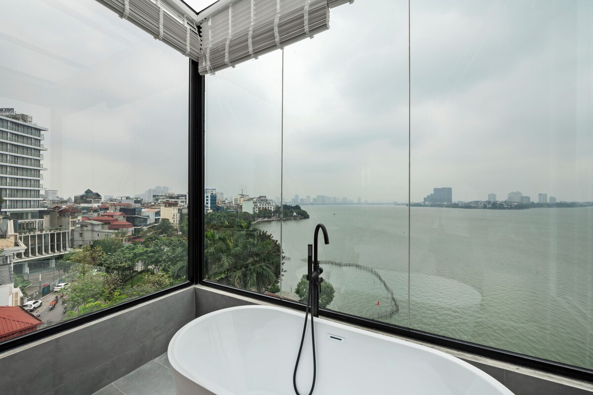 Une salle de bain moderne avec une grande baignoire, une vue sur une rivière et un paysage urbain en arrière-plan.