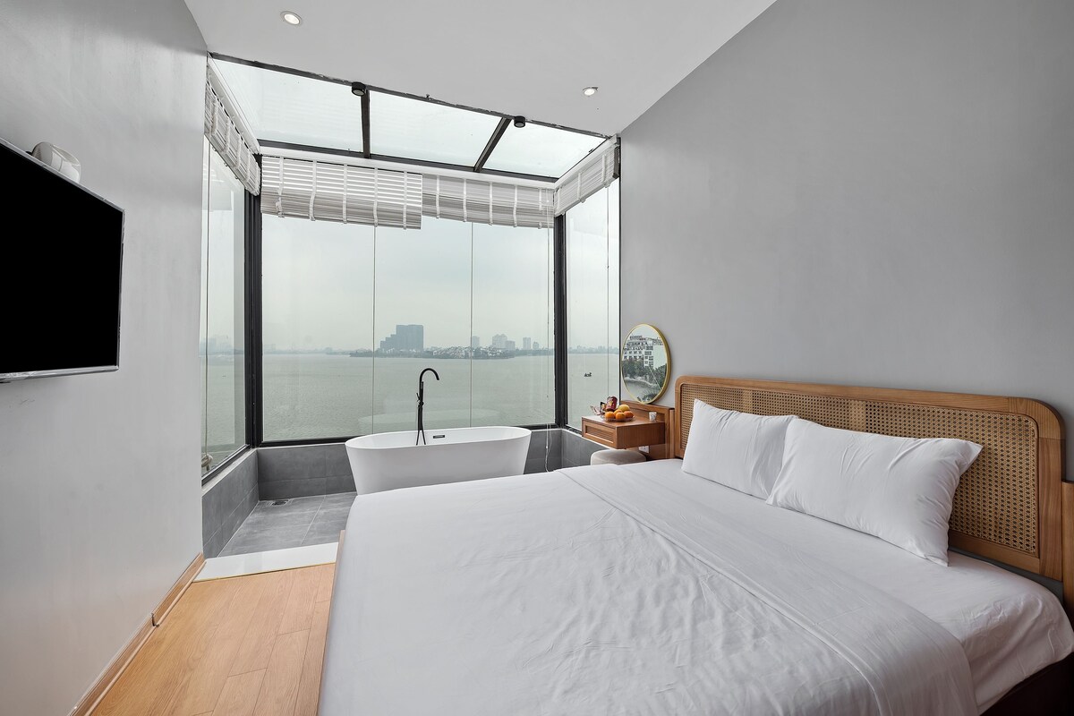 A modern bedroom with a large bed, a skylight, a bathtub, and a city view.