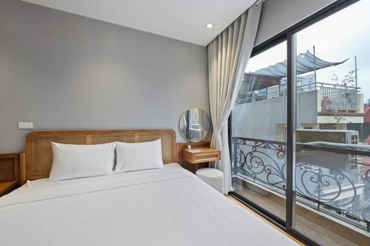Une chambre d’hôtel avec un grand lit, une tête de lit en bois, une table de chevet, un miroir rond et un balcon offrant une vue sur la ville.