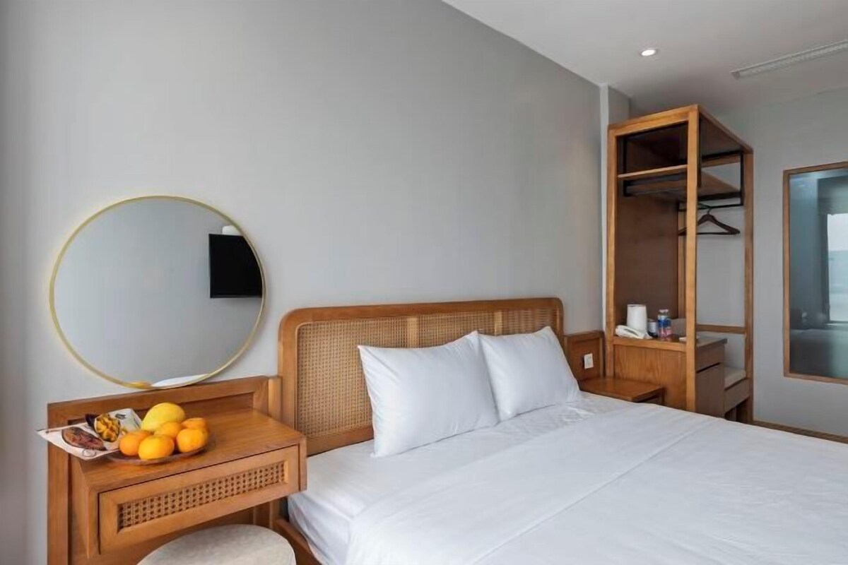 Une chambre d’hôtel avec un lit, une table de chevet sur laquelle se trouve un panier de fruits, un miroir et une armoire en bois.