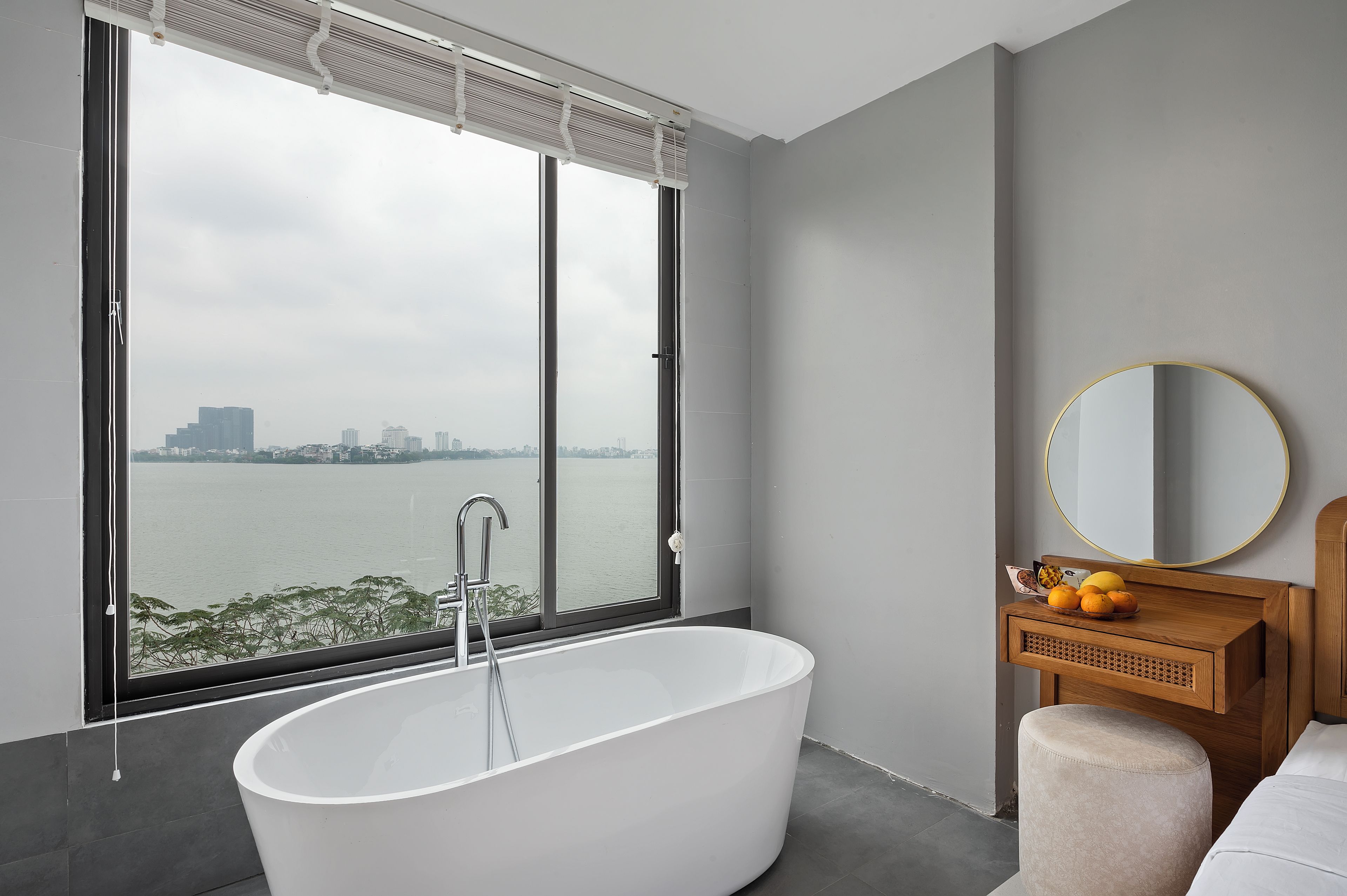 Une salle de bain moderne avec une baignoire sur pieds, un meuble-lavabo en bois avec un miroir rond et une vue sur le paysage urbain à travers une grande fenêtre.