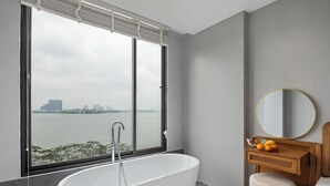 Une salle de bain moderne avec une baignoire sur pieds, un meuble-lavabo en bois avec un miroir rond et une vue sur le paysage urbain à travers une grande fenêtre.