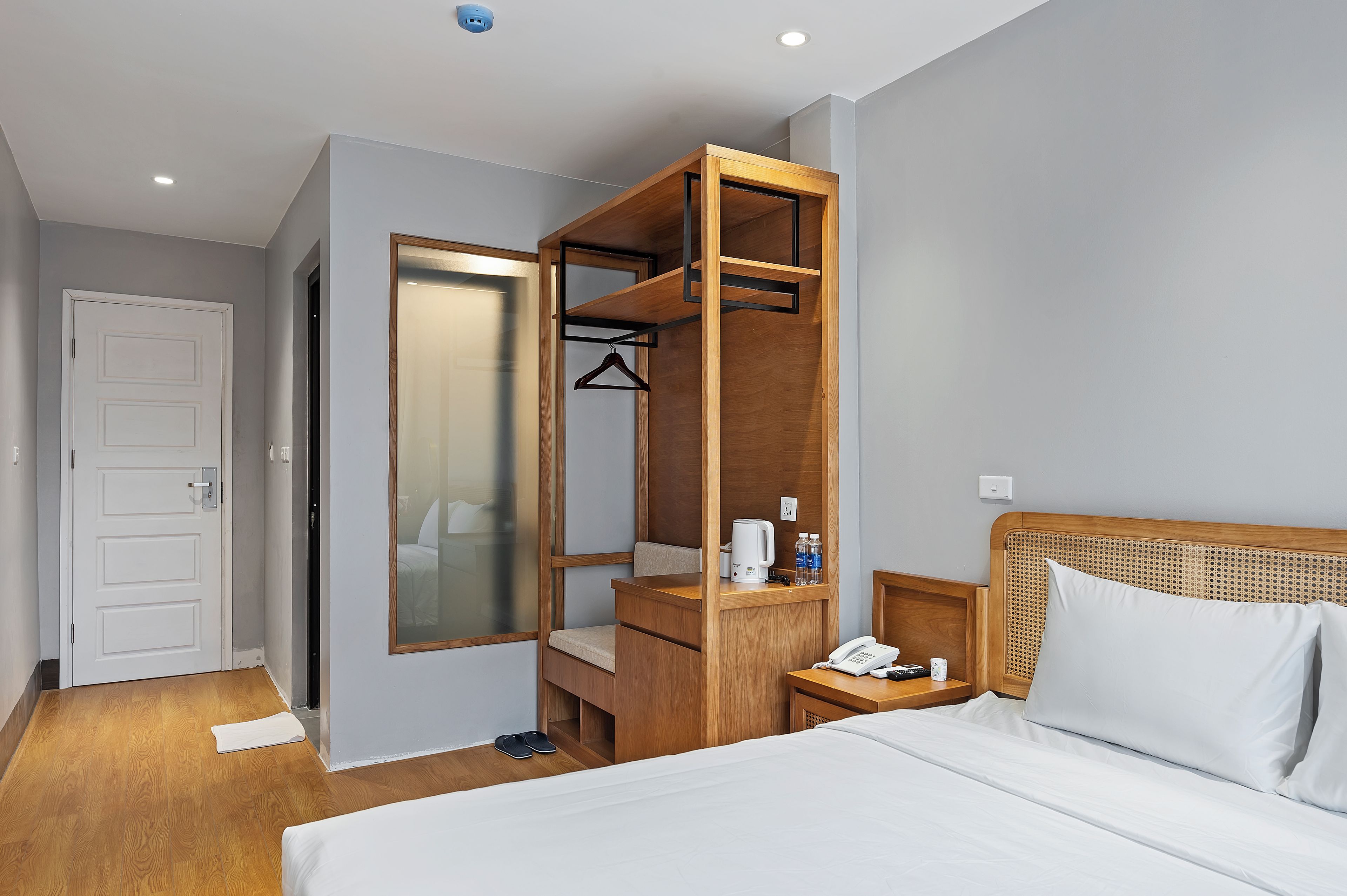 Une chambre d’hôtel comprenant un lit, une armoire en bois, une table de chevet avec un téléphone et une petite étagère avec des articles de toilette.