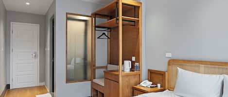Une chambre d’hôtel comprenant un lit, une armoire en bois, une table de chevet avec un téléphone et une petite étagère avec des articles de toilette.