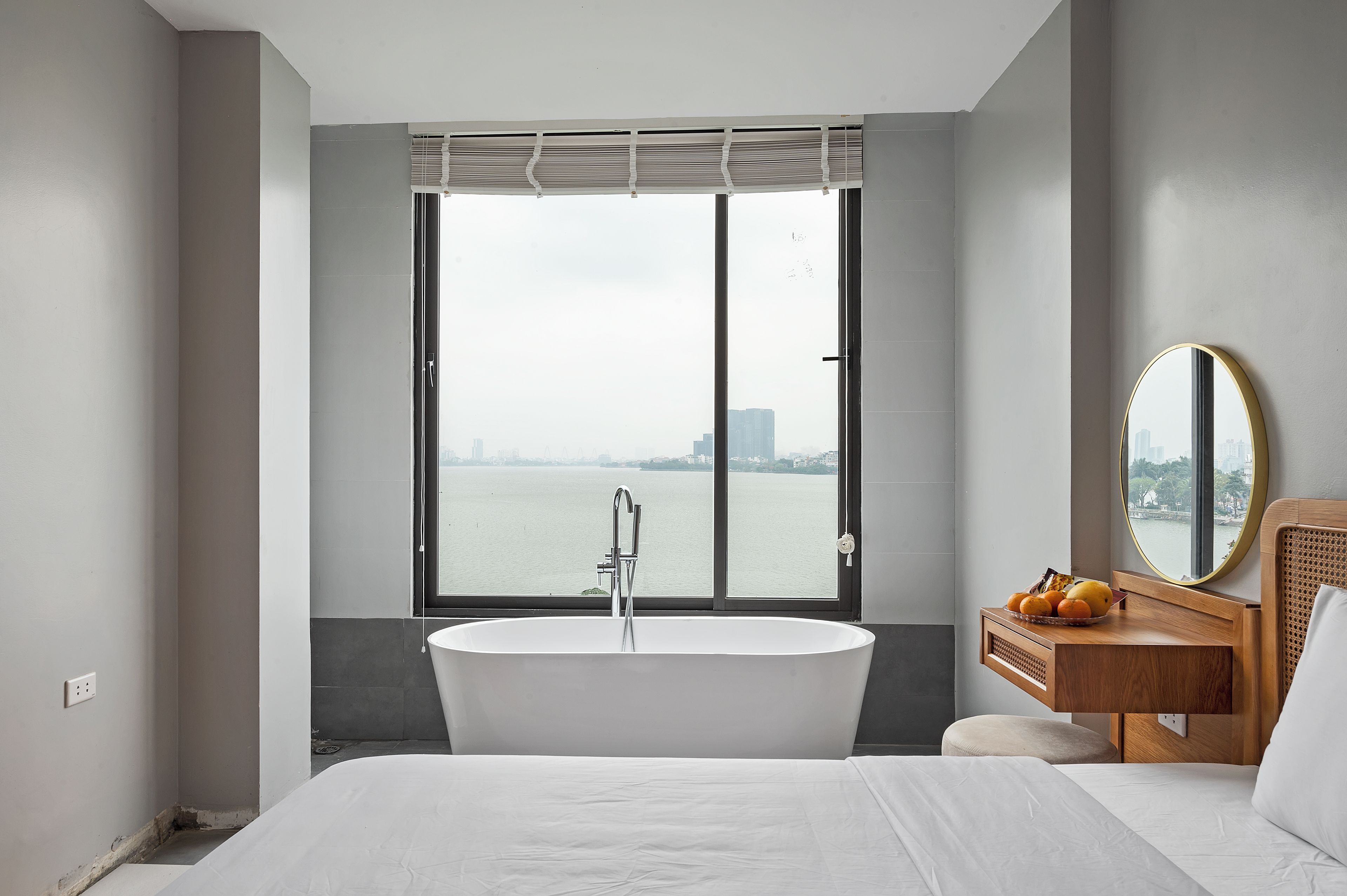 A modern bathroom with a freestanding bathtub, a wooden vanity with a mirror, and a large window offering a view of a cityscape.