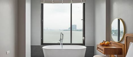 A modern bathroom with a freestanding bathtub, a wooden vanity with a mirror, and a large window offering a view of a cityscape.