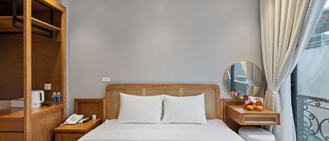 Habitación de hotel con cama, cabecero de madera, mesita de noche con teléfono, una pequeña mesa con espejo y una ventana con cortinas.