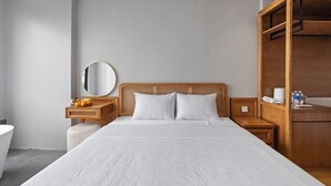 Une chambre d’hôtel moderne avec un grand lit, une tête de lit en bois, une table de chevet avec une lampe, une petite armoire en bois et un miroir rond accroché au mur.