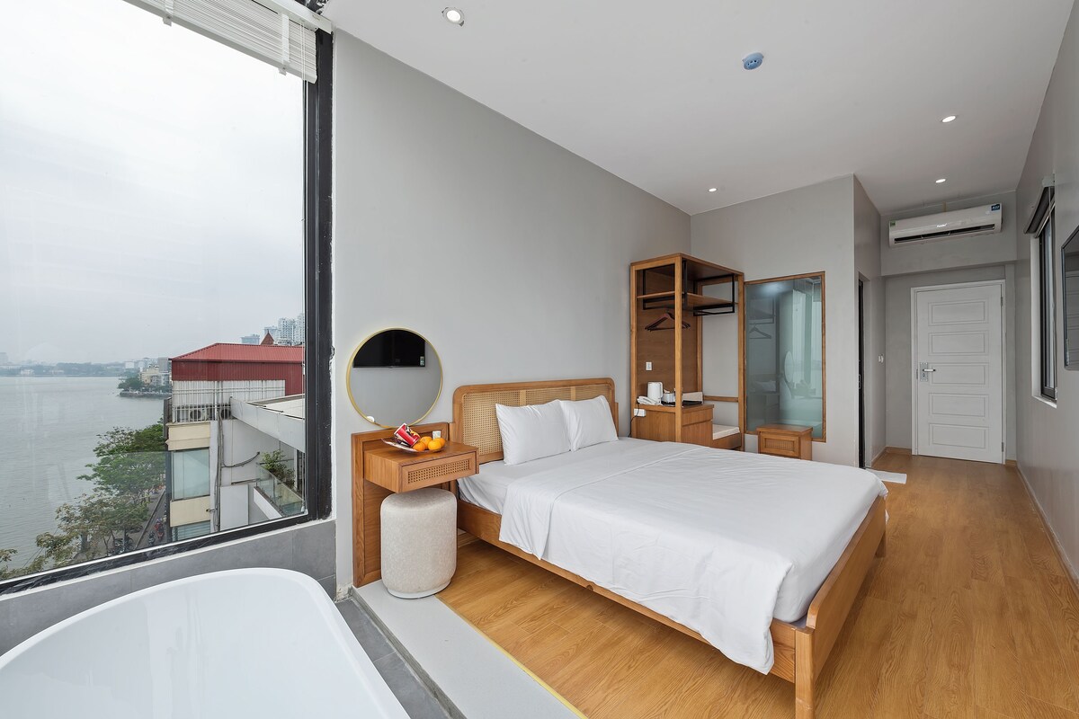 Et moderne hotelværelse med en stor seng, et natbord med et spejl, et klædeskab og udsigt til et vandareal.