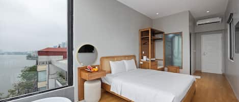 Una habitación de hotel moderna con una cama grande, una mesita de noche con espejo, un armario y vistas a una masa de agua.