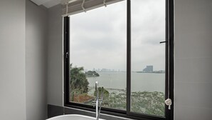 Une salle de bain moderne avec une baignoire sur pieds, une grande fenêtre offrant une vue sur le paysage urbain et un plan d’eau.