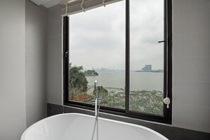 A modern bathroom with a freestanding bathtub, a large window with a view of a cityscape and water body. - Lakeview Residence (Hanoi)