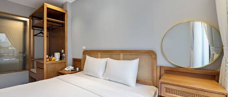 A hotel room with a bed, a wooden wardrobe, a bedside table with a phone, a round mirror, and a small seating area.