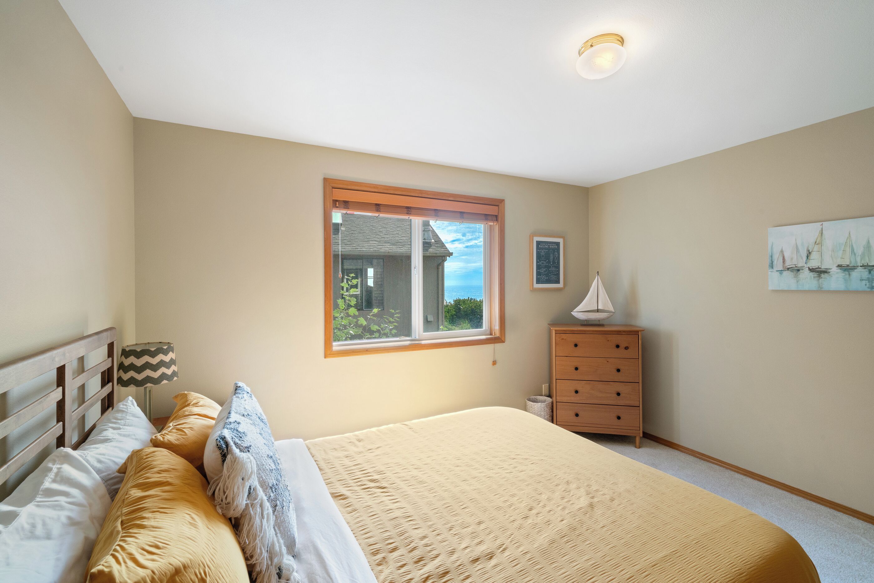 A bedroom with a bed, a dresser, a lamp, a window, and a painting on the wall.