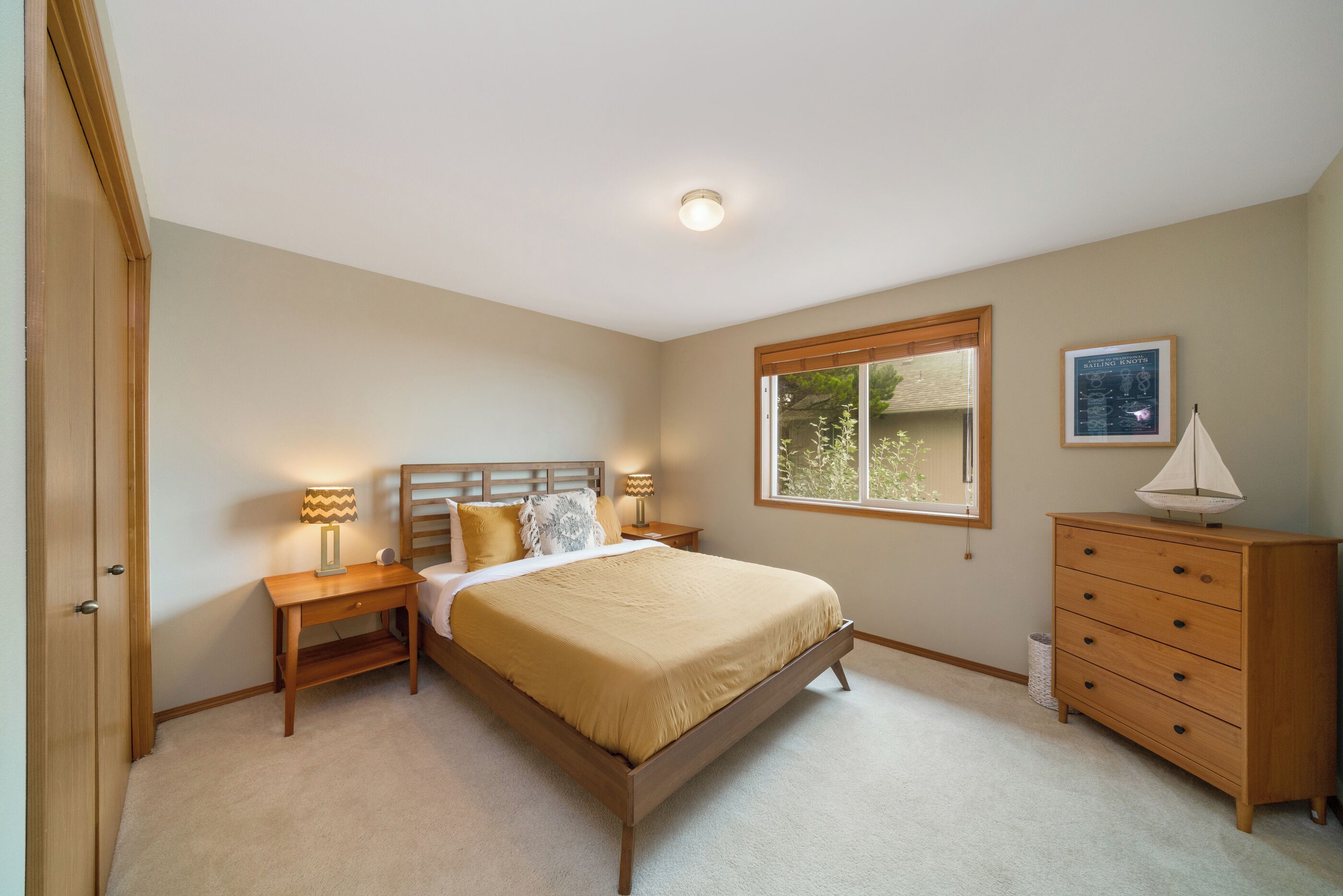 A bedroom with a bed, nightstands, a dresser, a window, and a ceiling light.