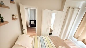 A bedroom with a bed, a wardrobe, a mirror, and a window with curtains.