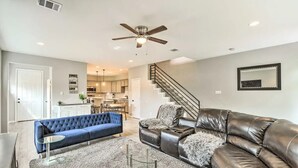 A spacious living room with a blue sofa, a leather sectional, and a glass coffee table. A ceiling fan and recessed lighting are visible. - 3BD Houston Home: Fenced Yard & Minutes to Downtown Houston (Houston)