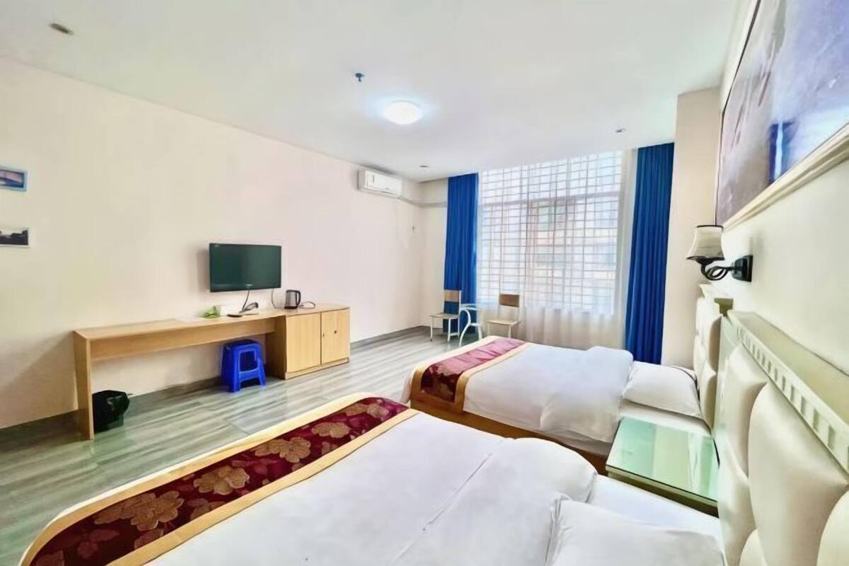 Hotellihuone, jossa on kaksi sänkyä, työpöytä, televisio ja ikkuna, jossa on verhot.