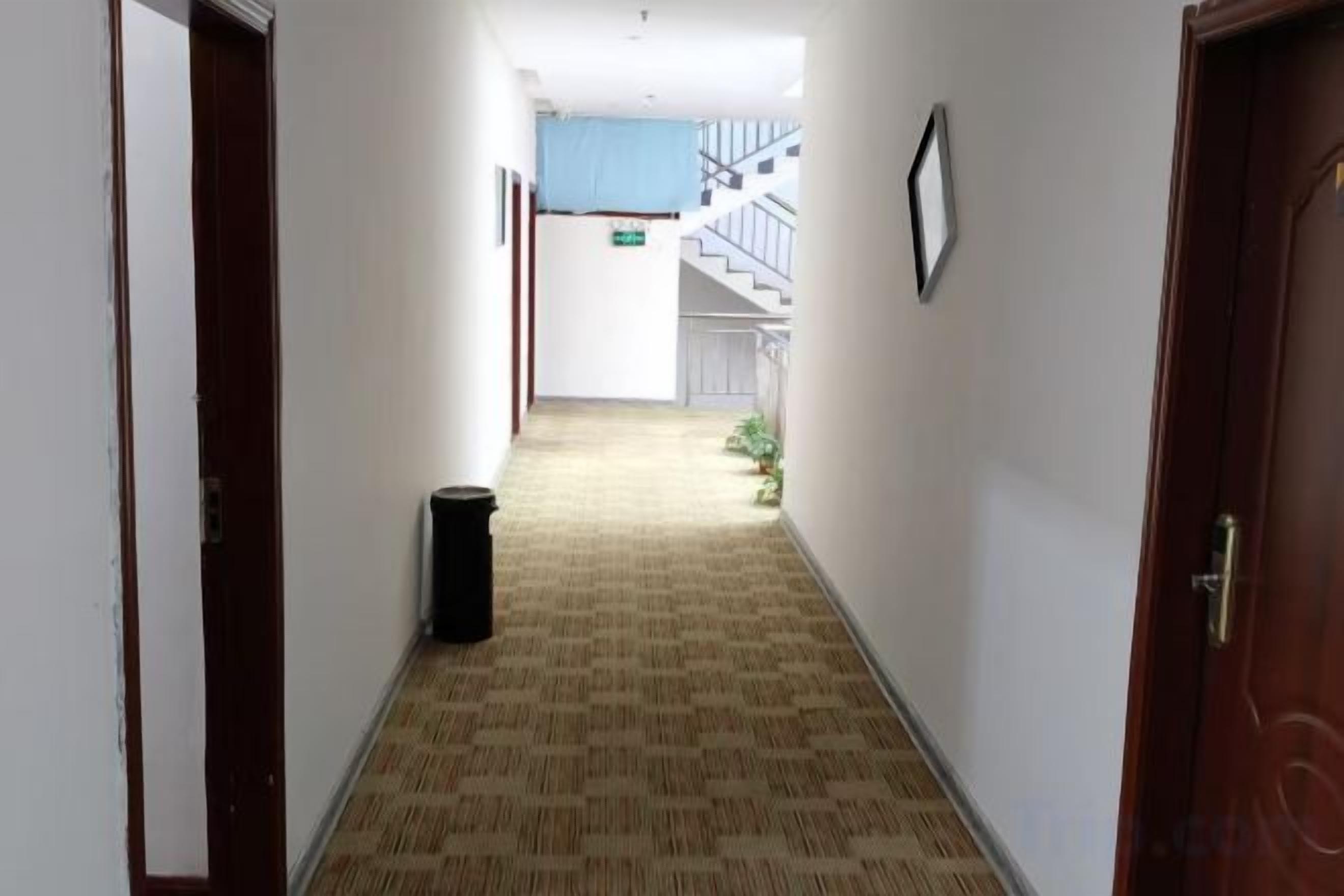 A hotel hallway with carpeted flooring, a trash bin, and a staircase in the background.