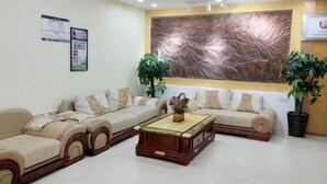 A reception area with a sofa set, a coffee table, two potted plants, and a large abstract painting on the wall. - Jingxi Guoyu Convenience Hotel (Jingxi)