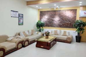 A reception area with a sofa set, a coffee table, two potted plants, and a large abstract painting on the wall. - Jingxi Guoyu Convenience Hotel (Jingxi)